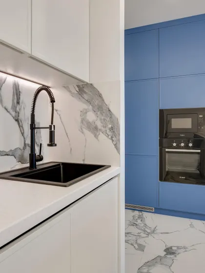 A modern kitchen design that plays with contrast, featuring white countertops and a marble backsplash against bold blue floor-to-ceiling cabinets with integrated appliances.