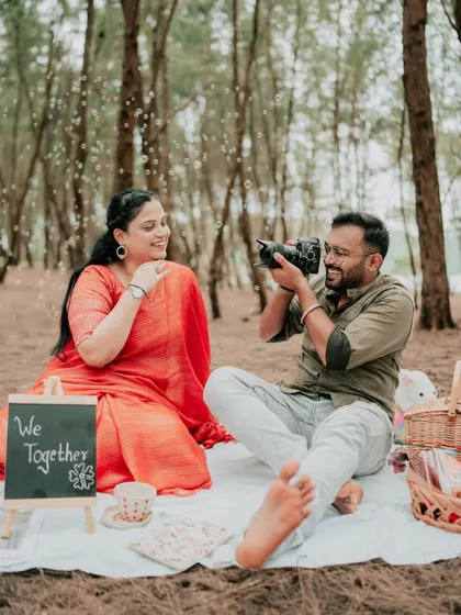 A playful moment during a picnic-themed pre-wedding shoot, with the groom pretending to photograph the bride.