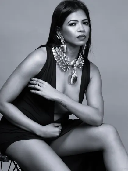 A dramatic black and white portrait of a model in a plunging black dress, adorned with a statement necklace. The lighting is moody and cinematic.