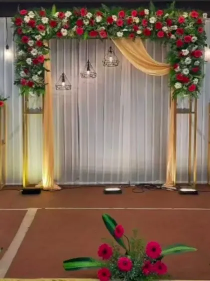 A simple and modern engagement backdrop with a square arch, industrial-style hanging lights, and red and white floral accents.
