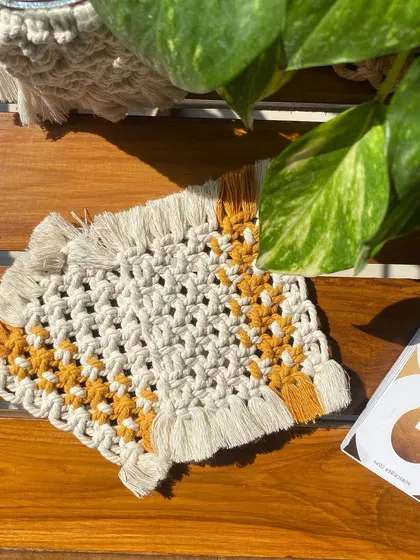 A close-up of the beige and yellow square macrame coaster, perfect for a modern or boho-chic living space.