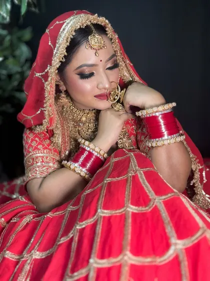 A candid moment captured. The bride is looking down, showcasing her beautiful glittery eye makeup and the rich red of her bridal lehenga.