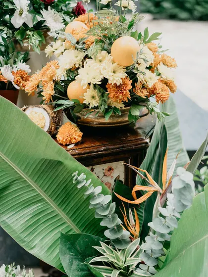 A tropical and vibrant floral arrangement featuring oranges, banana leaves, and birds of paradise flowers.