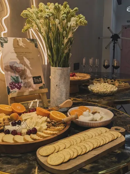 A stylish wine and cheese setup for an event at Trims and Tones salon. The marble tables are adorned with cheese boards, crackers, and glasses of red wine, creating a chic and sophisticated atmosphere.