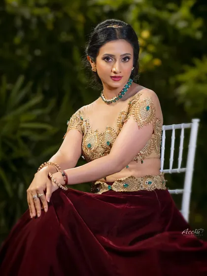 A seated portrait that feels classic and royal. The outdoor greenery provides a beautiful, natural backdrop for the rich colors of the maroon and gold lehenga.