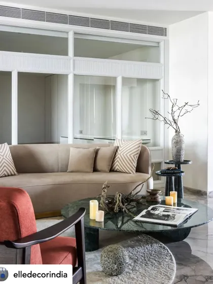This view showcases the room's architecture, with elegant white-framed glass partitions that create an open, airy feel. The mix of a neutral curved sofa and a bold red armchair adds dynamic interest.