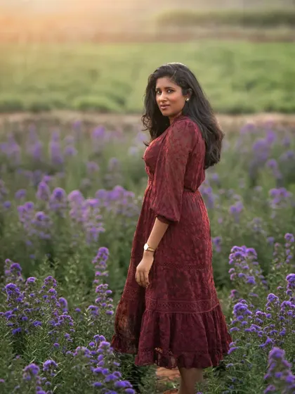 A woman in a deep red dress stands in a field of purple flowers. The soft, golden light of sunset creates a dreamy and romantic atmosphere, making this a beautiful and evocative outdoor portrait.