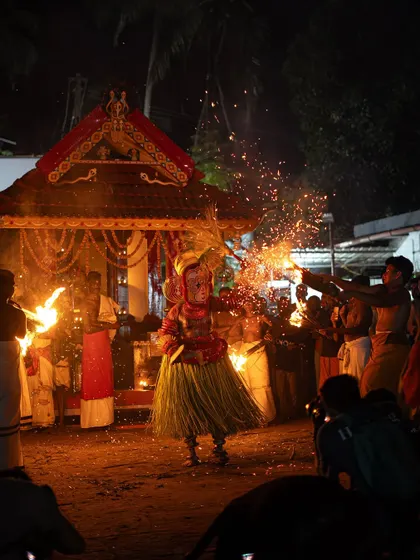Images of the Pottan Theyyam dancing with torches in front of a small temple, or palliyara. The sparks flying around him create a mesmerizing spectacle of light and motion.