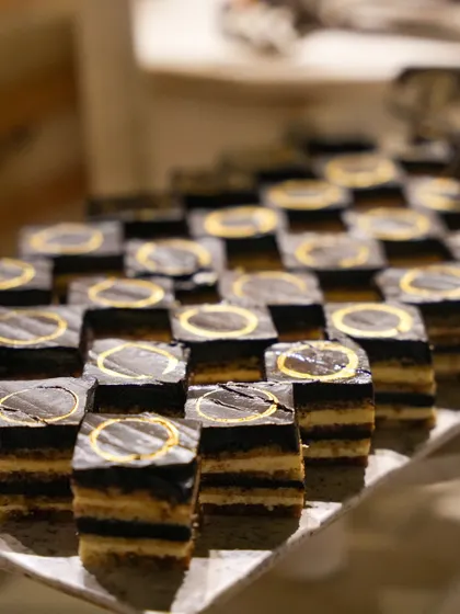A tray of our opera cake petit fours, each adorned with a gold-dusted chocolate seal. This small detail adds a touch of luxury and branding to our desserts.