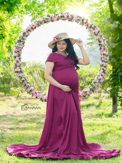 A serene portrait of a mother-to-be in a wine-colored gown and hat, framed by a circular floral prop.