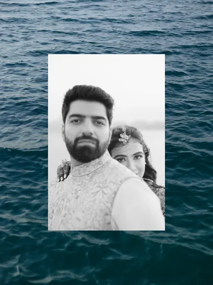 A creative black and white portrait of a couple by the sea, framed by the deep blue water.