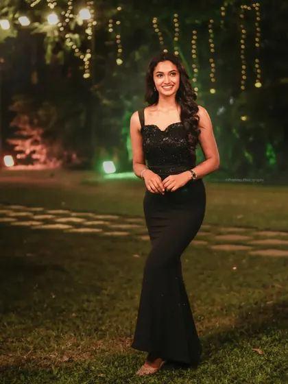 A full-length portrait of actress Reeshma Nanaiah in a black gown at an outdoor event. This shot showcases her elegance against a beautifully lit natural background.