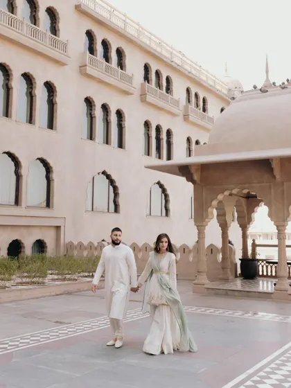 Amani and TJ walk hand-in-hand through the courtyard of the Fairmont Jaipur. The beautiful architecture provides a perfect frame for their elegant, coordinated attire.