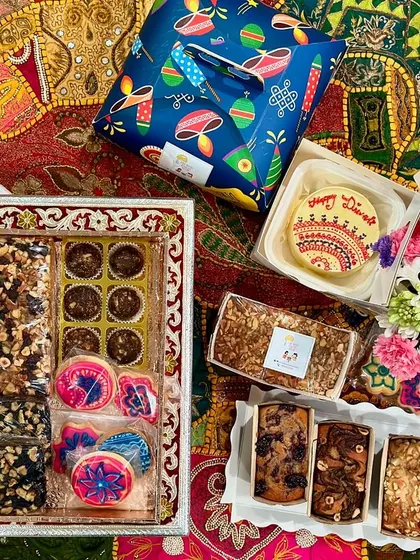 A complete celebration spread showcasing the variety we offer. This custom Diwali hamper includes a hand-decorated bento cake, assorted tea cakes, themed icing cookies, chocolate nut clusters, and fresh flowers, all arranged beautifully for gifting.
