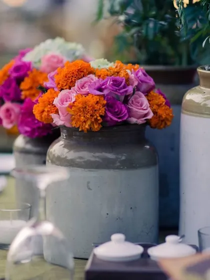 A centerpiece featuring a mix of vibrant marigolds and roses in a traditional ceramic pot. This is a classic look for festive Indian events.