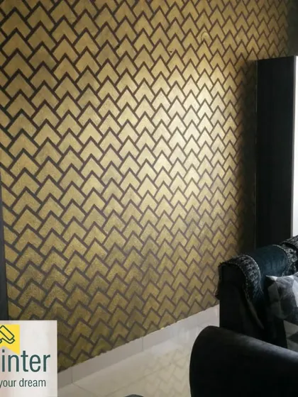 A striking geometric pattern in gold and charcoal gives this living room wall a modern, art-deco feel. This is an example of a metallic texture finish that catches the light beautifully.
