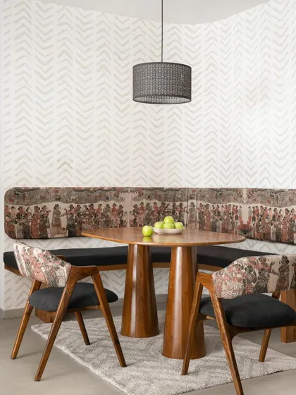 This cozy dining nook from our 'Palaash' project features a custom curved wall with built-in seating. The bold tribal-print upholstery and teak wood table create a unique and intimate space for family meals.