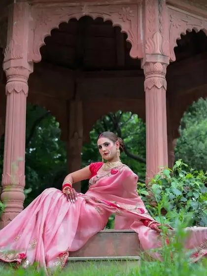 A relaxed and confident seated pose in the gazebo. The model's expression is serene, and the natural light enhances the soft pink of her saree.