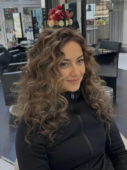 An elegant color transformation on naturally curly hair. The soft highlights are carefully placed to enhance the dimension and shape of her beautiful curls.