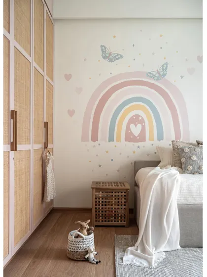Creating a dreamy haven for a spirited 3-year-old, we embraced her love for pink. The room features a grey sofa bed, blush pink rattan wardrobes, and a hand-painted pastel rainbow on the wall.