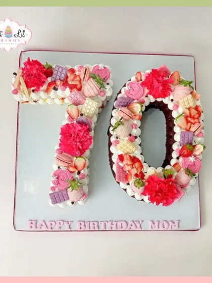 A beautiful number cake for a 70th birthday. The "70" is decorated with pink and white frosting, fresh strawberries, and chocolates.