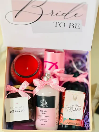 A look inside a 'Bride to be' gift box. It's filled with pampering items like body lotion, a scented candle, and other treats, all in a cheerful pink theme.