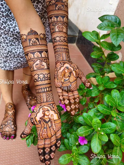 A complete bridal look featuring Karwa Chauth scenes. This design includes portraits of a couple performing rituals, extending up the arm with architectural and floral details.