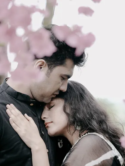 An intimate and romantic close-up of a couple, framed by soft pink flowers, creating a dreamy and tender portrait.