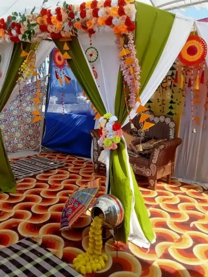 A canopy-style mandap for a Haldi or Mehendi ceremony, decorated with green and white drapes, floral arrangements, and traditional props like a silver 'matka'.