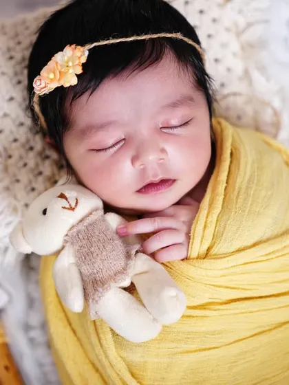 A sweet sleeping baby girl with a floral headband, holding a tiny teddy bear. This home session was so peaceful.