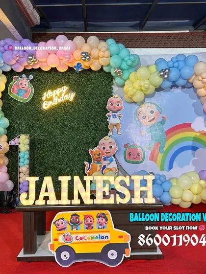 Jainesh's Cocomelon first birthday party. This setup features a grass wall backdrop, a pastel balloon arch, and light-up letters spelling the name.