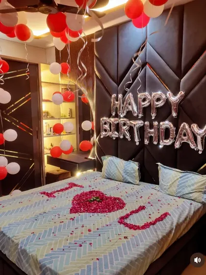 A close-up of the bed with a rose petal heart and 'I LOVE YOU' message, against a modern, upholstered headboard.