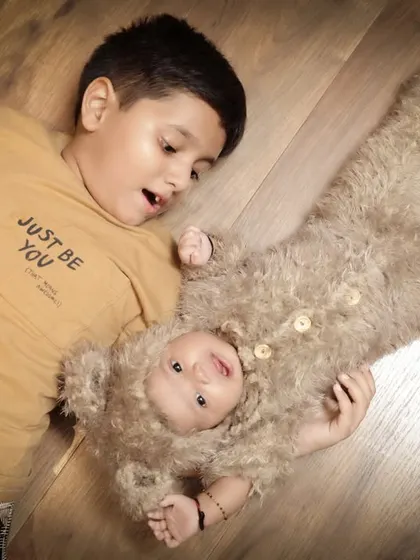 A playful interaction between brothers. The older brother looks with delight at his baby brother, who is dressed as a little bear.