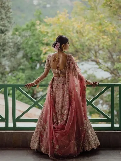 The bride looks out from a balcony overlooking the lush green hills and lake, her pastel lehenga a soft contrast to the vibrant nature.