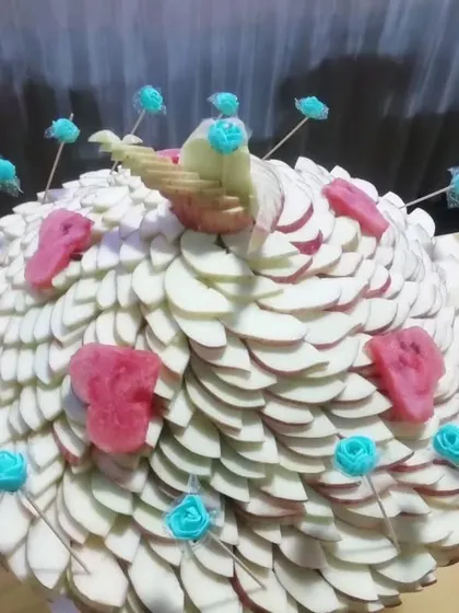 A peacock-inspired fruit sculpture made from sliced apples and decorated with watermelon and sugar roses. This is an example of my bespoke fruit carving services.