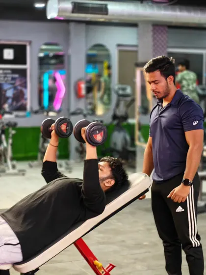 A trainer supervises a client performing an incline dumbbell press. We keep a close watch on your form to maximize muscle engagement and prevent injury.