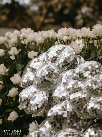 A cluster of disco balls nestled in a bed of classic white roses, a surprising and playful combination of textures and styles.