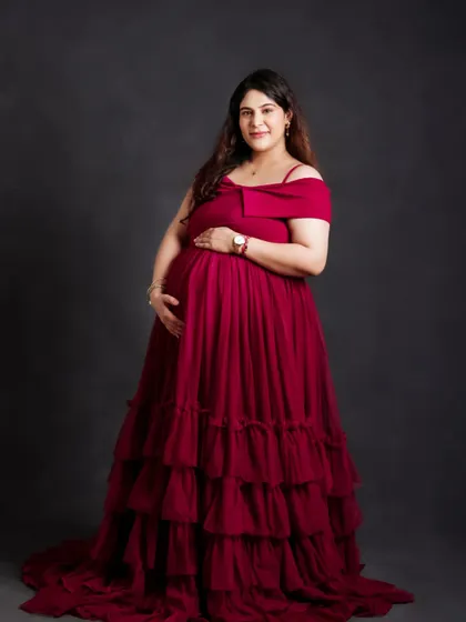 A classic portrait showcasing a gorgeous, deep red tiered gown. The off-shoulder design and rich color beautifully complement the mom-to-be's radiant glow.