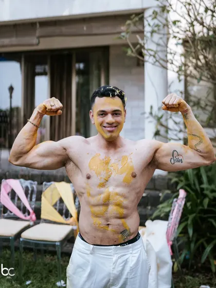 The groom proudly showing off his physique, playfully smeared with haldi after the main rituals are done.