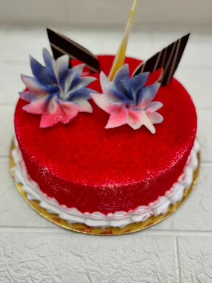 A vibrant and classic Red Velvet cake. The striking red sponge is complemented by a simple cream cheese frosting and topped with beautiful, edible floral decorations.
