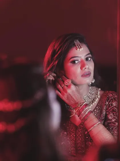 A dramatic, beautifully lit shot of my bride Sahana getting ready for her reception. The red lighting adds a touch of drama to her red and grey lehenga look.