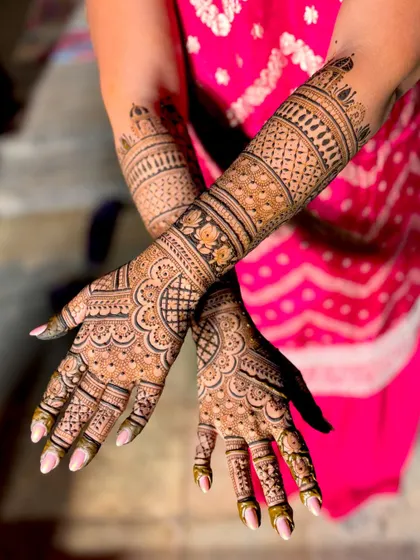 A crossed-hands view of another detailed bridal mehendi, showcasing the rich patterns.