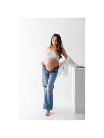 A graceful leaning pose that feels both natural and chic. The simplicity of the white shirt and jeans keeps the focus on the beautiful baby bump.