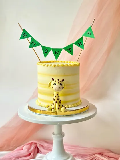 An 18-month celebration cake with a cute fondant giraffe and a striped buttercream finish.