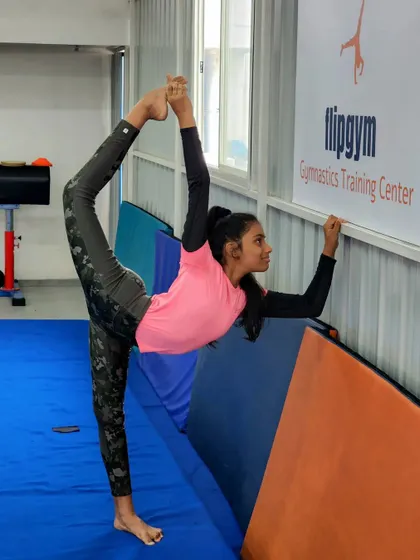 A close-up of a student perfecting her needle scale against the wall, a challenging pose that requires immense flexibility.