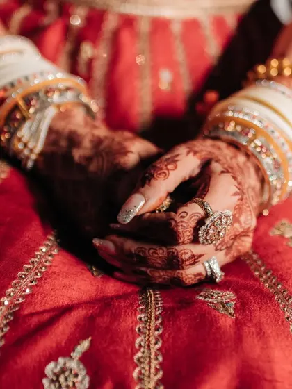 A close-up of the bride's hands, showcasing her intricate henna design and contrasting ivory chooda (bangles), a modern twist on a traditional bridal accessory.