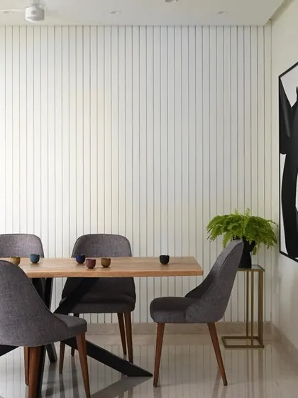 Simplicity can be very powerful. This dining area uses a clean, minimalist aesthetic with a beautiful wood table and comfortable grey chairs. The vertically grooved wall paneling adds subtle texture and visual interest without cluttering the space.