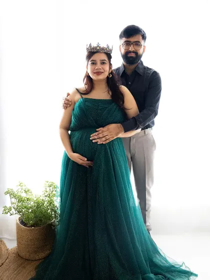 A regal portrait of a couple, with the mom-to-be wearing a crown and a beautiful green gown, smiling at the camera.
