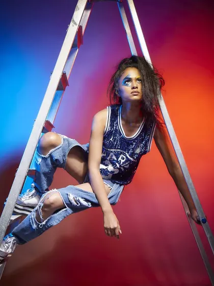 An artistic, high-energy shot for Diseno.in, with the model posed on a ladder against a red and blue background.