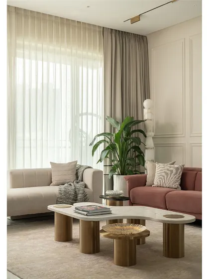 Natural light floods this living room, highlighting the soft textures of the rug and sofas. The layout is designed to be open and conversational, with a mix of curved and clean-lined furniture creating a balanced and harmonious feel.